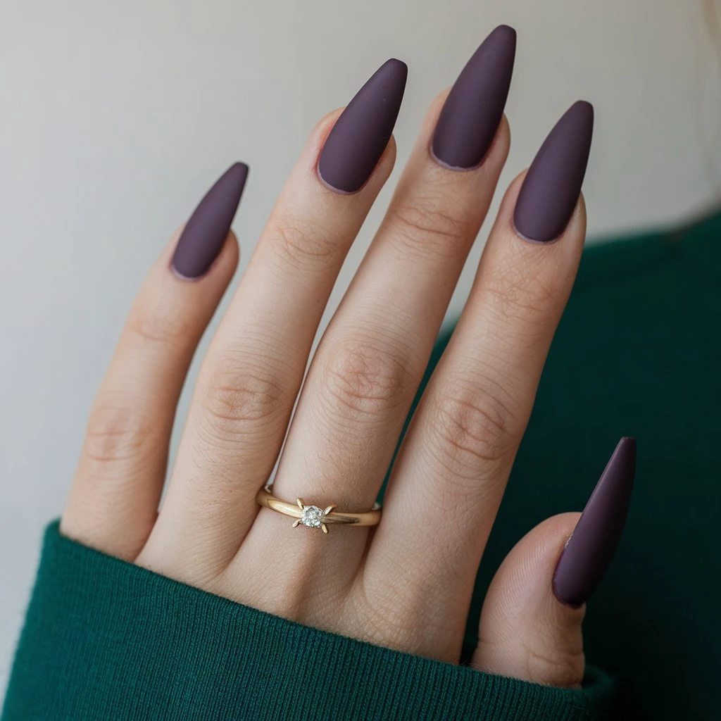 The image shows a close-up of a woman's hand with short, pointed nails. The nails are painted Vampy Purple with Matte Finish and have a glossy finish.